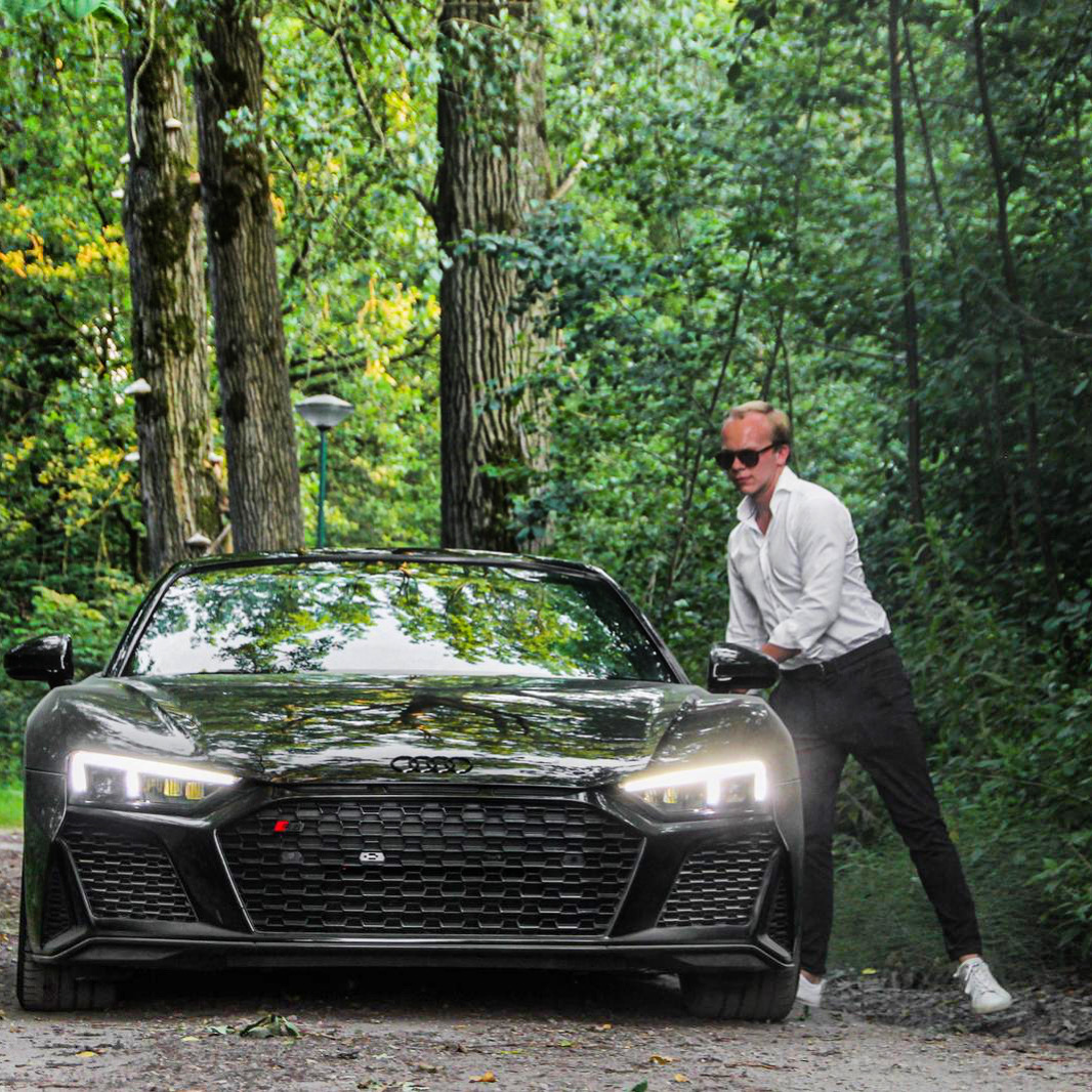 Joris next to a black Audi R8 on a forest road.